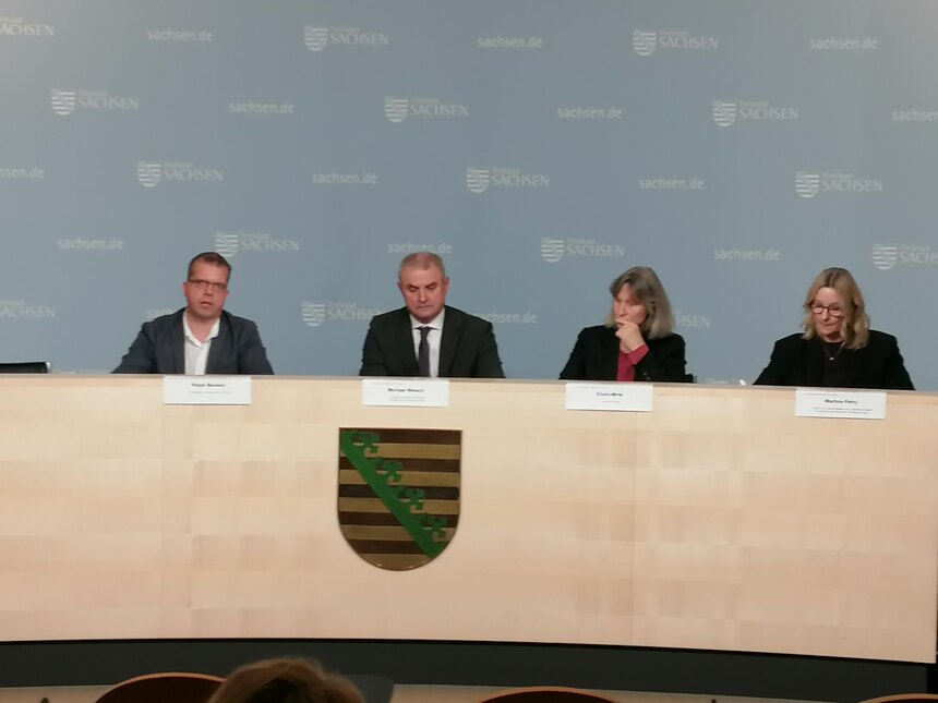 Podium: vier Personen frontal zu sehen, zwei Männer und zwei Frauen