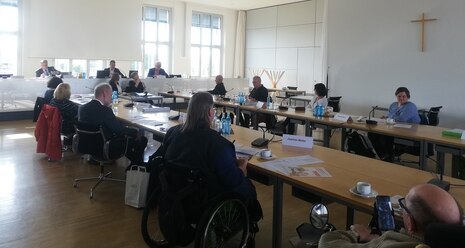 Sitzungsrunde mit Podium, Teilnehmer sind Frauen und Männer, sie blicken zum Podium